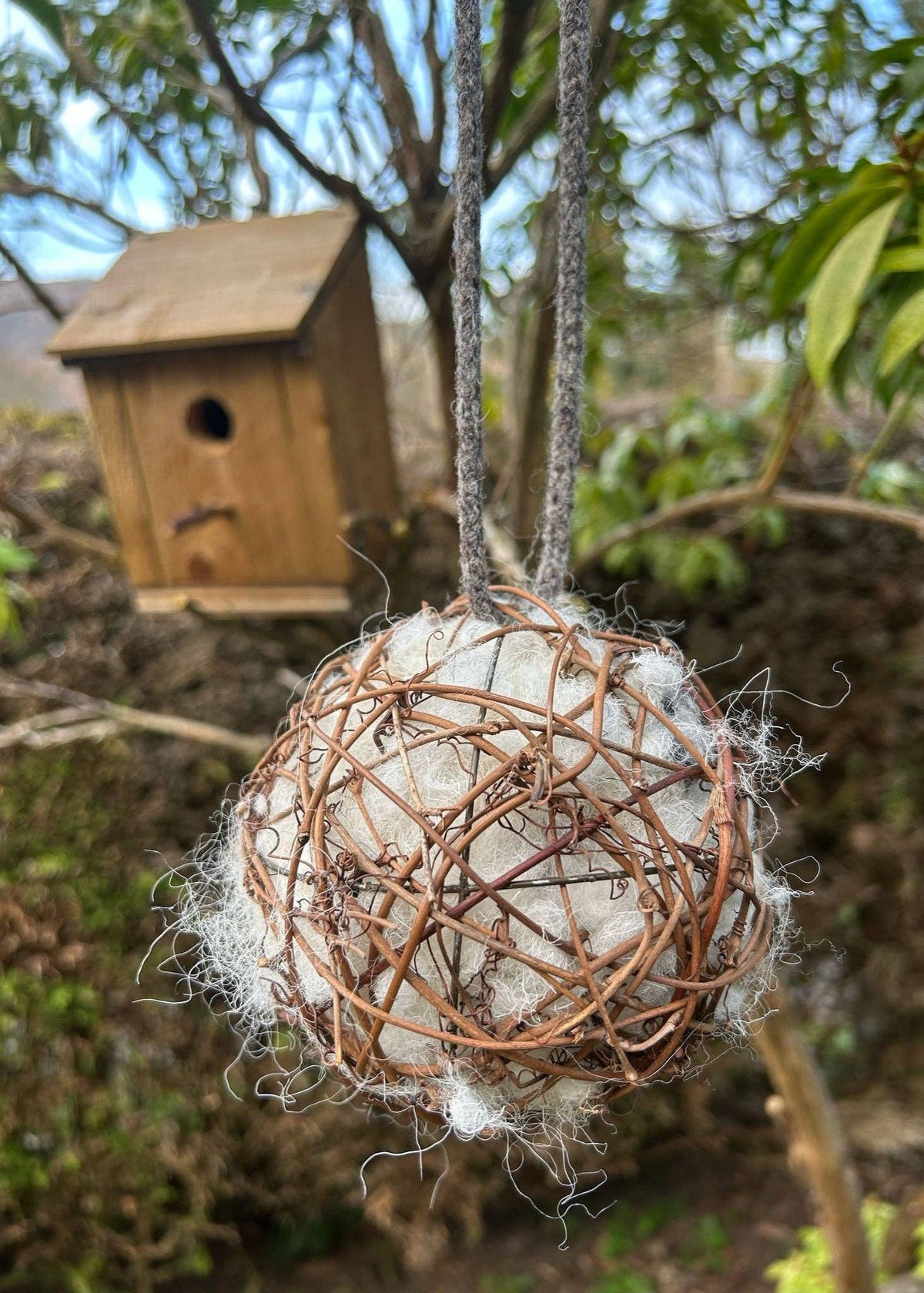Natural sheep's wool nesting ball for garden birds hanging near a wooden birdhouse