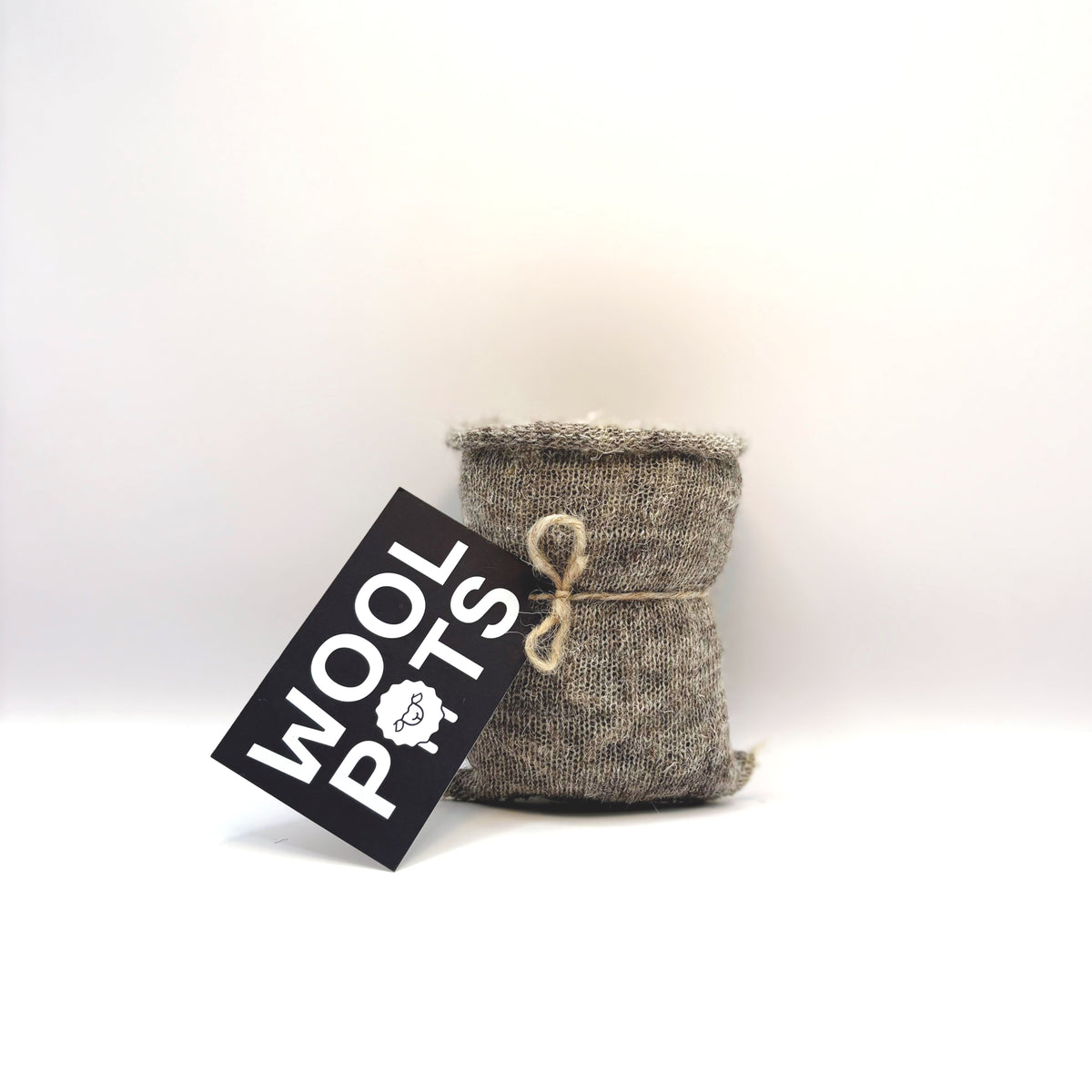 A small woven wool pot in a heathered gray and brown textured fabric, tied with a natural jute twine bow, with a black hanging tag that reads WOOL POTS on a white background.