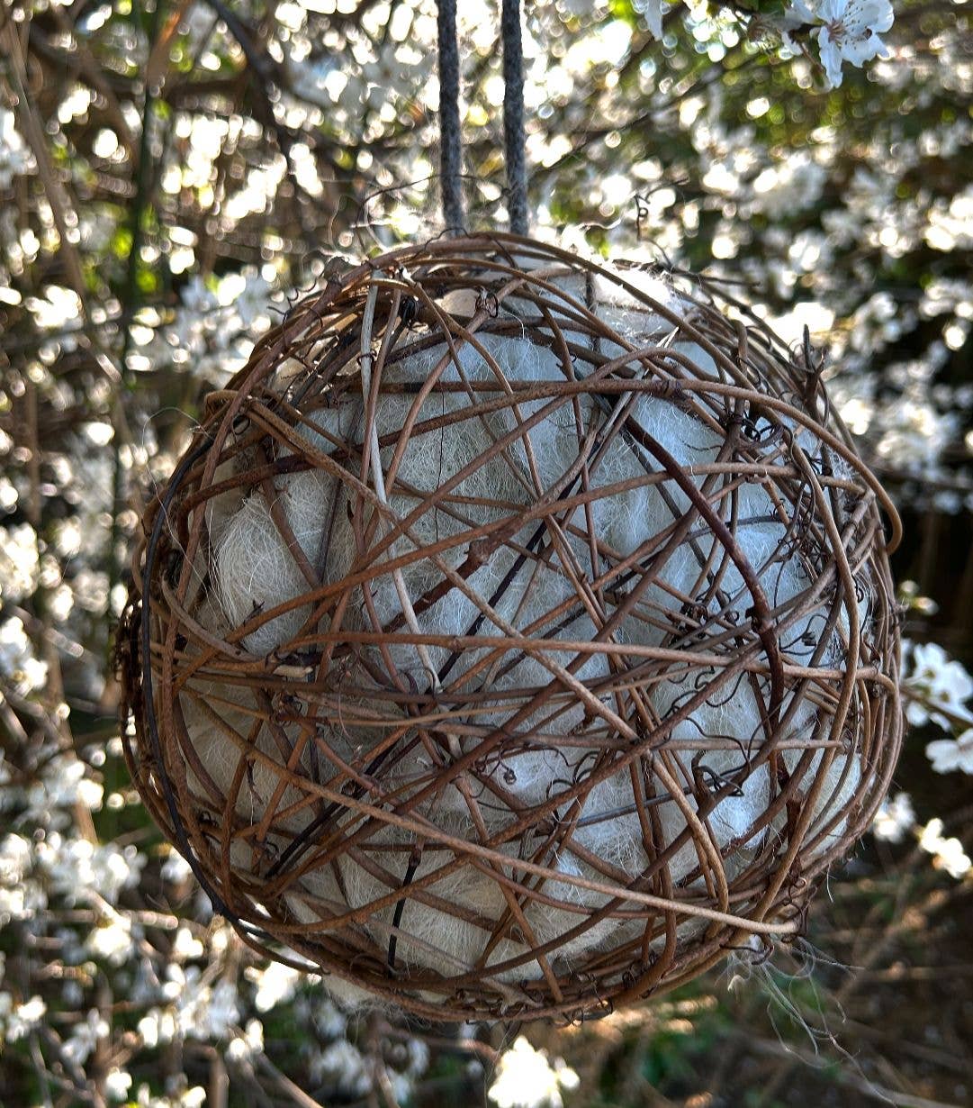 Natural sheep's wool nesting ball 20cm with dark woven willow hanging in a tree