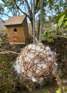 Natural sheep's wool nesting ball for garden birds hanging near a wooden birdhouse