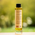 Golden TranQuillina Calendula Oil in a clear glass bottle with a natural garden background