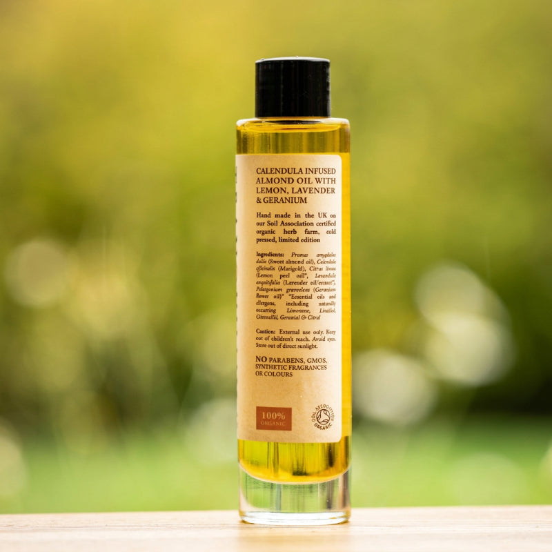 Golden TranQuillina Calendula Oil in a clear glass bottle with a natural garden background